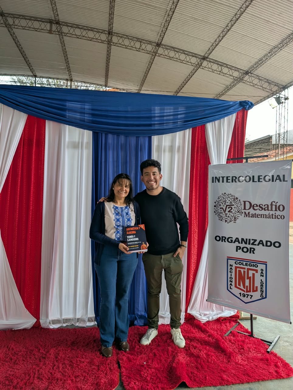 Ricardo Romero junto a una docente con el Tomo 1 en el Intercolegial Desafío Matemático del Colegio Nacional San Lorenzo